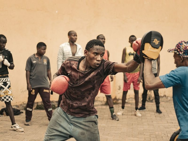 Boxtraining im Freien: ein Jugendlicher schlägt in die Pratzen, umringt von der Gruppe