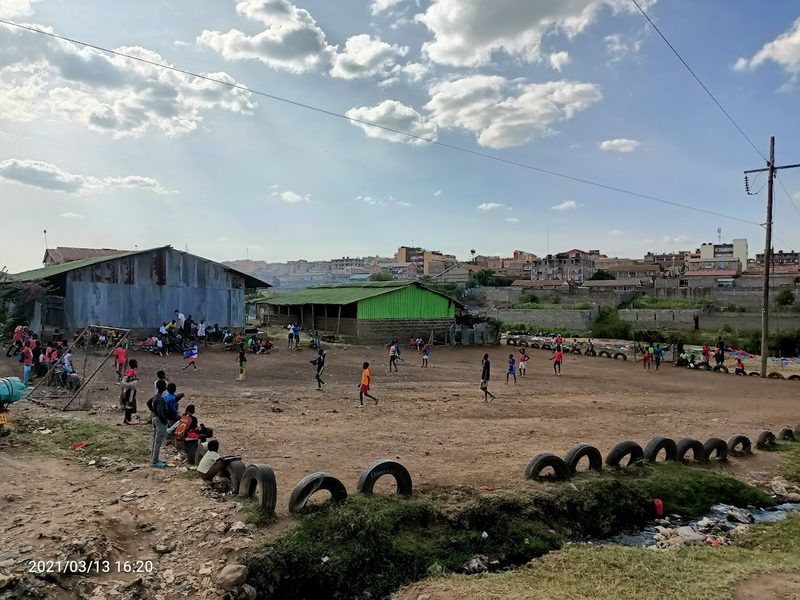 Fussballplatz aus Erde, mit Autoreifen abgegrenzt, Kinder spielen darauf, Dandora im Hintergrund